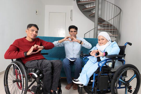 Three people sitting on a couch with one person in a wheelchair.
