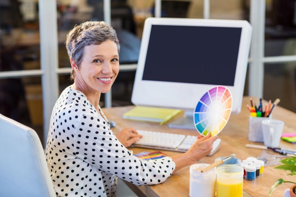A woman sitting at a table with a computer and color wheel.