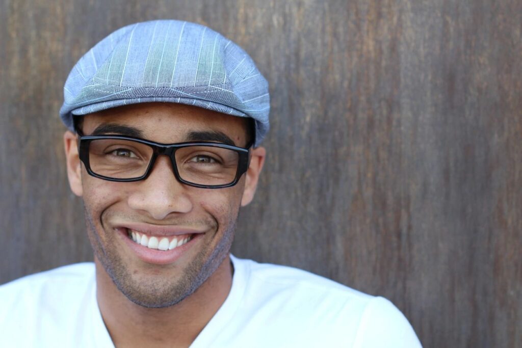 A man wearing glasses and a hat smiling.